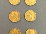 six gold sovereigns of different sizes and shapes on a gray surface