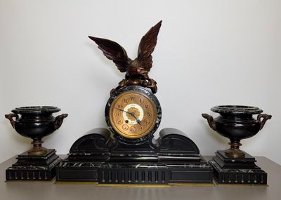 a clock with an eagle on top of it next to two vases