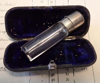une petite bouteille en verre posée dans un étui, sur une feuille de papier