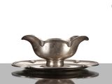 une assiette en argent ancien posée sur une soucoupe, le tout reposant sur une surface réfléchissante