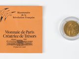 a gold coin next to a booklet on a white surface