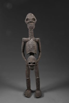 une figurine en bois représentant un squelette tenant un crâne entre ses mains