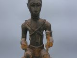 une vieille statue en bois représentant un homme assis sur une chaise