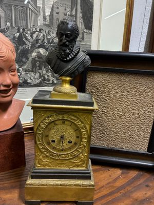 un buste d'homme assis à côté d'une horloge posée sur une table