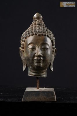 une tête de Bouddha en bronze posée sur un socle en bois