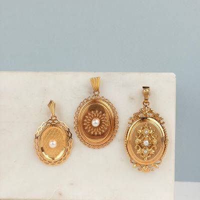 trois boucles d'oreilles en or et un pendentif en perle posés sur un bloc de marbre