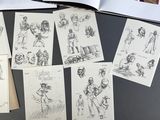 a bunch of drawings on a table with a book open