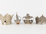 four silver crowns are lined up in a row on a white surface