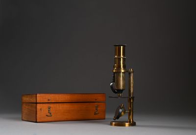 un vieux microscope en laiton posé sur une table, dans un coffret en bois