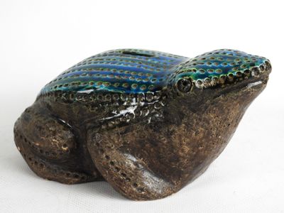 une petite grenouille en céramique posée sur une surface blanche