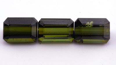 un gros plan sur trois perles de tourmaline verte posées sur une surface blanche