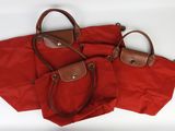trois sacs rouges avec des anses marron, posés sur un fond blanc