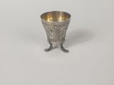 une coupe en argent ancien posée sur un socle, sur une surface blanche