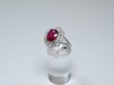 an oval ruby and diamond ring on a clear glass stand