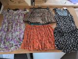 quatre robes posées sur une table, avec des piles de cartons en arrière-plan
