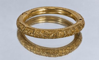 two gold bracelets with intricate designs on them on a white surface