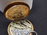 une petite boîte blanche contenant une montre de poche en or