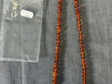 un collier de perles orange et un sac en plastique transparent posé sur un tissu gris