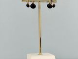 des boucles d'oreilles dorées et noires posées sur un socle en marbre, lui-même posé sur une table en marbre