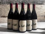 six bottles of wine are lined up on a table in front of a stone wall