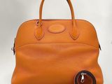 un sac à main en cuir orange avec une bandoulière marron et un fond blanc