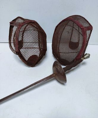 une paire de masques d'escrime et une crosse posés sur une surface blanche