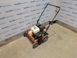 an orange and black lawn mower sitting in front of a blue and white wall