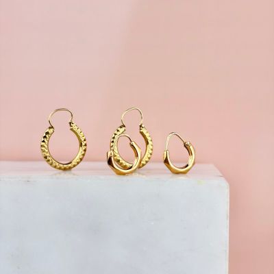 une paire de boucles d'oreilles en anneau en or posée sur un bloc de marbre