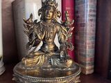a statue of a person sitting on a bowl on a shelf