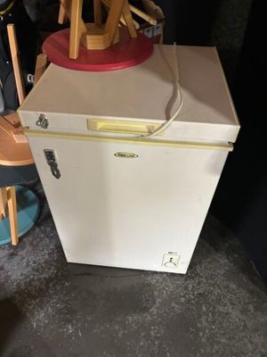 a small white refrigerator with a red top and a wooden chair