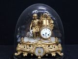 a gold clock under a glass dome on a black surface