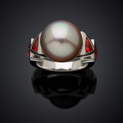 a close up of a pearl and ruby ring on a black surface