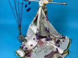 a white scarf with purple flowers on it next to a vase with purple flowers