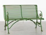 un vieux banc vert posé sur un sol en béton, près d'un mur blanc