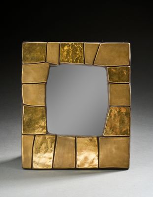 miroir carré doré posé sur une surface blanche avec un fond noir