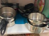 Plusieurs casseroles et poêles sont posées sur une étagère dans une cuisine.