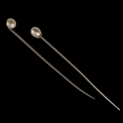 a pair of metal needles with pearls on them against a black background