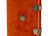 un carnet en cuir orange rehaussé de détails métalliques sur fond blanc