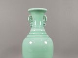 un vase vert posé sur une table, sur fond gris