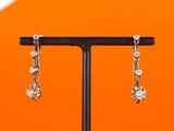 silver plated earrings on a black stand against an orange background