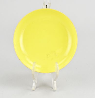 une assiette jaune posée sur un support transparent, sur une surface blanche