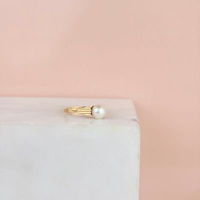 a gold ring with a pearl on top of a white marble block