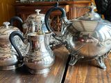 a cat sitting on a table next to a silver tea pot