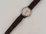 the watch is sitting on a white surface with a brown strap