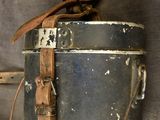 an old metal bucket with a leather strap hanging on a wall