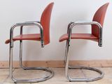 pair of red leather chairs sitting on a tiled floor in front of a white wall