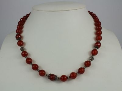 a close up of a necklace with red beads on a mannequin