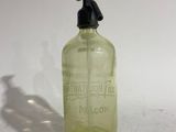 an old green glass bottle with a black cap on a white surface