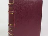 an old book with a red cover sitting on top of a white table