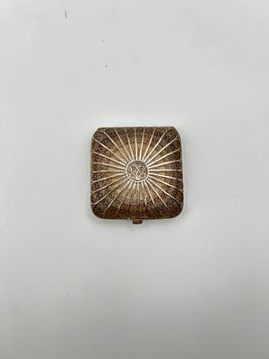 un petit objet métallique carré orné d'un motif en forme d'étoile rayonnante